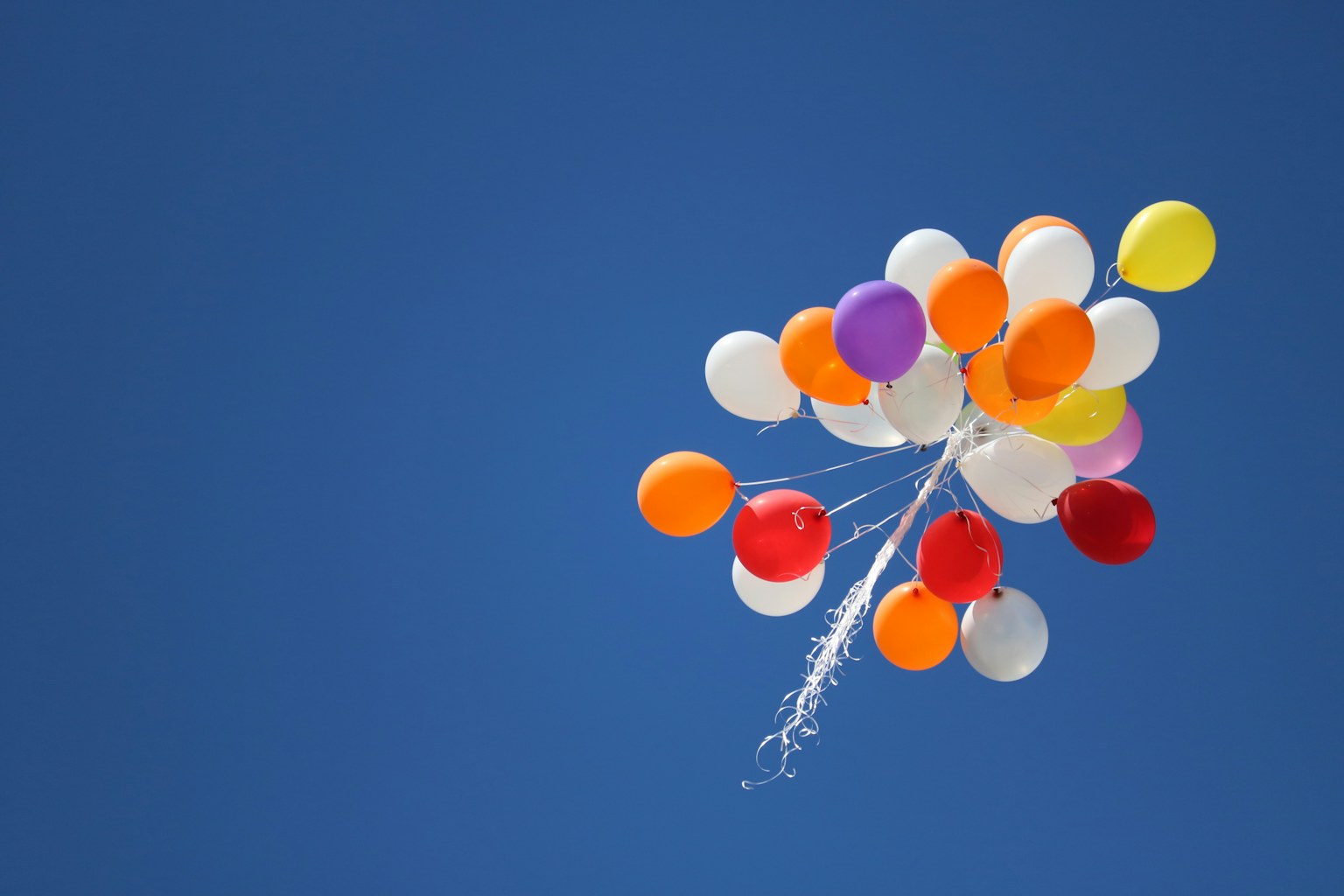 A bright bouquet of colourful balloons floating against a clear blue sky
