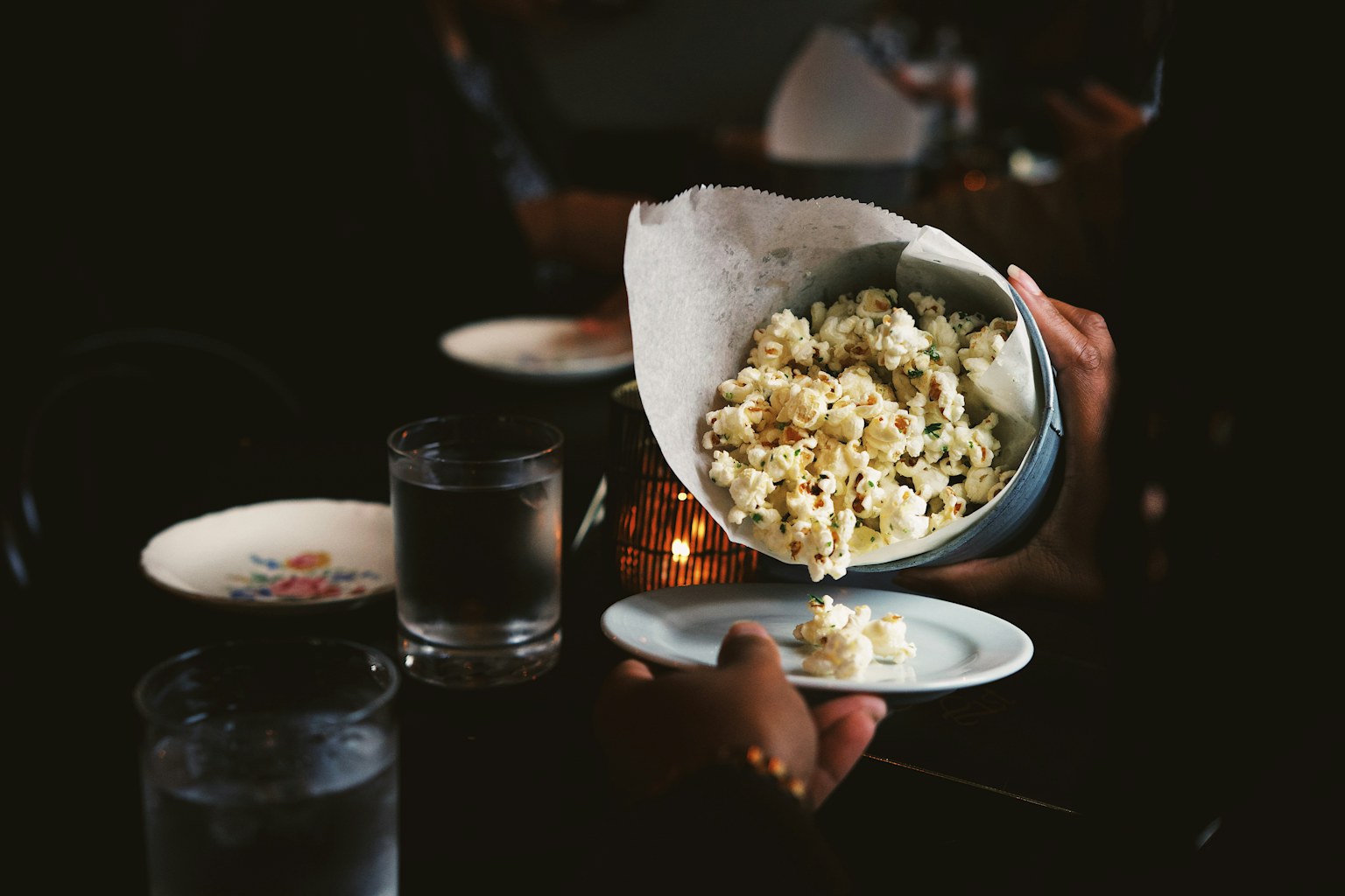 Hands sharing a bowl of popcorn across a warm, candlelit table